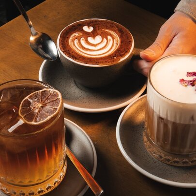 A top-down shot shows three different coffee beverages served on a dark wooden table.