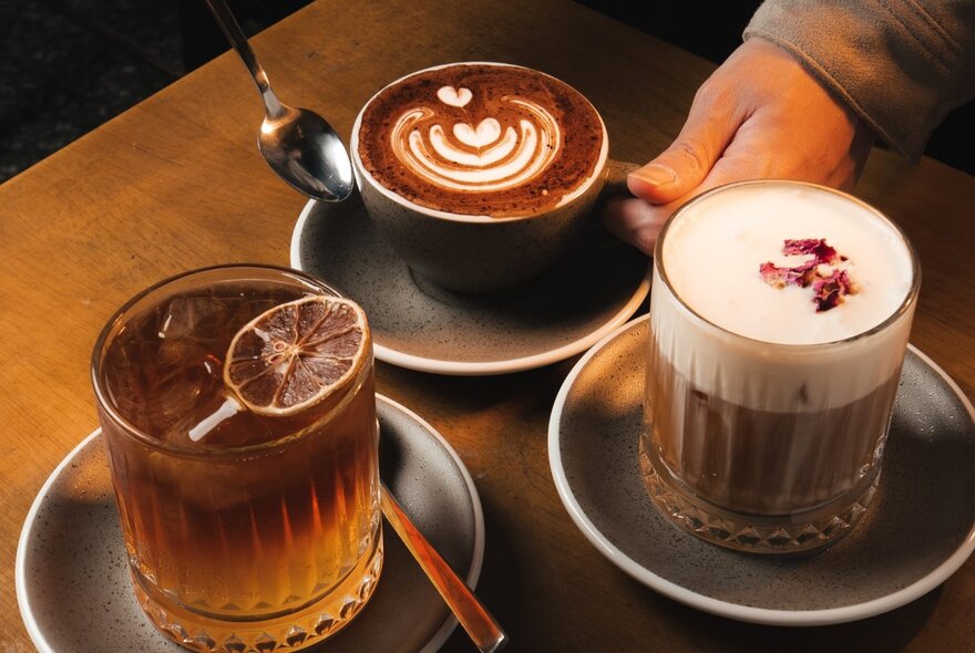 A top-down shot shows three different coffee beverages served on a dark wooden table.