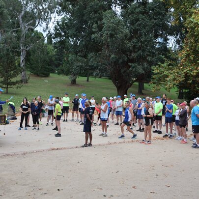 Group of runners in the Botanical Gardens at the Tan, listening to a speaker.