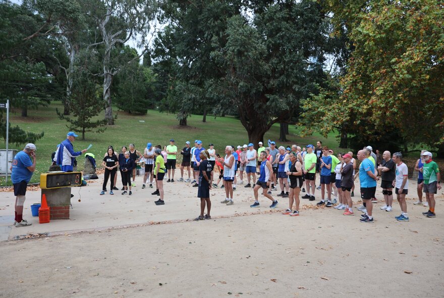 Group of runners in the Botanical Gardens at the Tan, listening to a speaker.