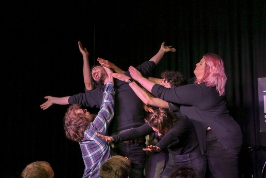 Group of people, on stage, learning over one person who appears to be fainting.