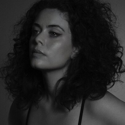 Moody, dark portrait of a young woman with shoulder-length dark hair.