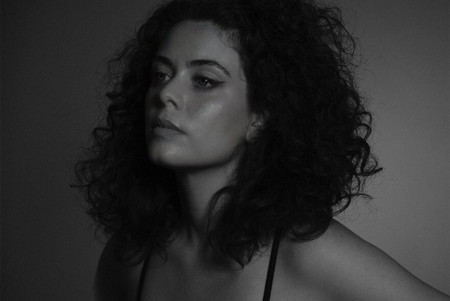 Moody, dark portrait of a young woman with shoulder-length dark hair.