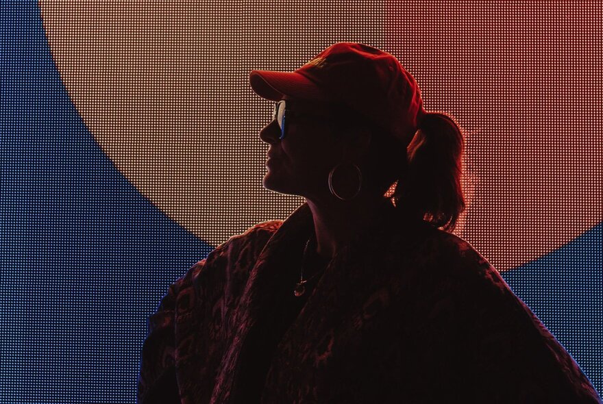 A shadowy silhouette of Melbourne musician DJ JNETT, wearing a cap and sunglasses.