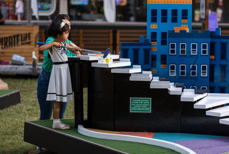 A child playing a minigolf game featuring a hill with steps.