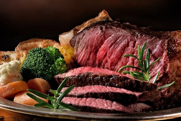 A platter of rare sliced roast beef, with roasted vegetables on the side.