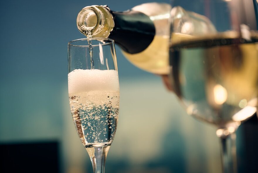 Sparkling wine being poured from a bottle into a champagne flute glass.