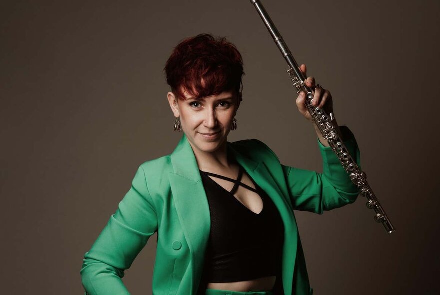 Classical flautist with her instrument in one hand, other hand on hip.