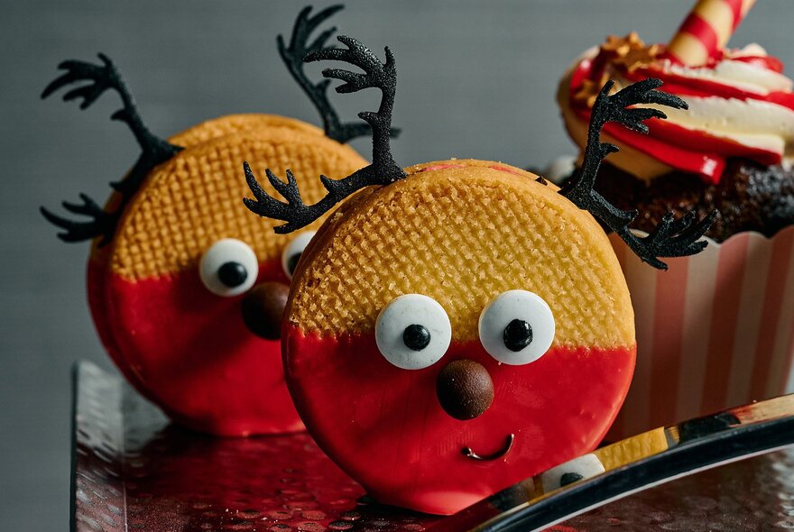 Two round cookies dipped in red icing decorated with eyes, nose, mouth and antlers to look like reindeer.