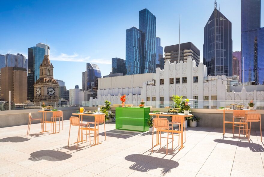 The roof terrace of Holiday Inn Bourke Street Mall with outdoor tables and chairs, a green bar area and views of the city skyline.