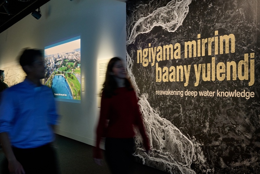 People passing an exhibition sign in a museum.