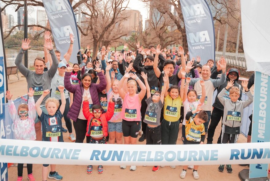 A group of kids with their hands up in front of a Run Melbourne banner. 
