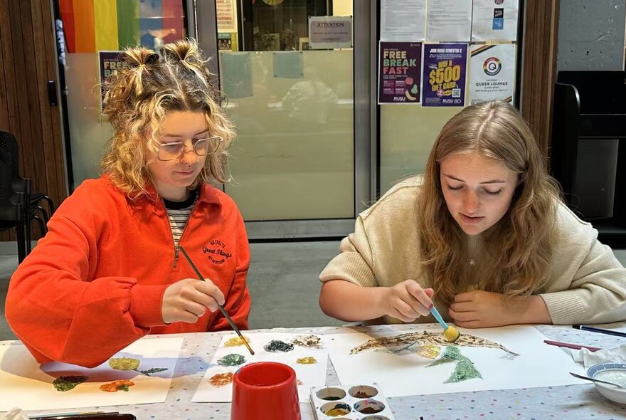 People seated at a table with paints and paper.