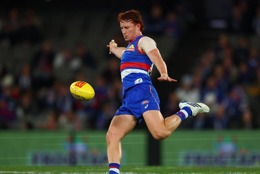 Western Bulldogs player Ed Richards goes for the kick, leg extended back and ball in mid air.