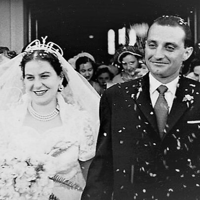 A vintage black and white photo dating from the mid-1950s, of a bride and groom leaving a church and being showered in confetti by onlookers.