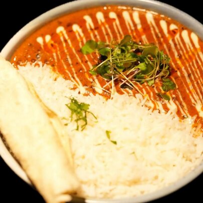 A bowl of dhal with rice and a rolled up naan bread, a drizzle of yogurt across the top.