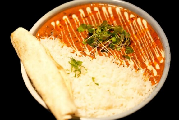 A bowl of dhal with rice and a rolled up naan bread, a drizzle of yogurt across the top.