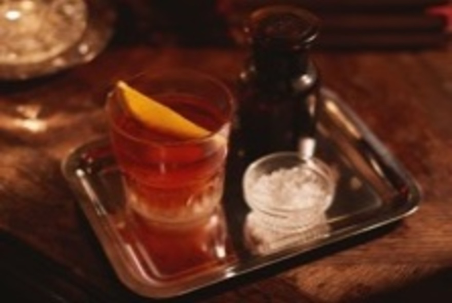 An orange coloured cocktail in a short tumbler on a silver tray.