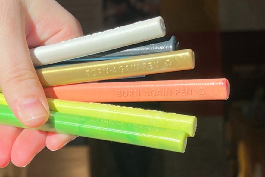 A hand holding a range of different coloured pens. 