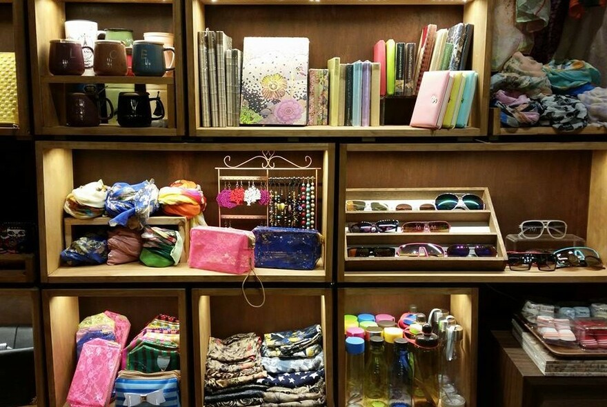 Three shelves in low light, featuring notebooks, sunglasses, bags and trinkets.