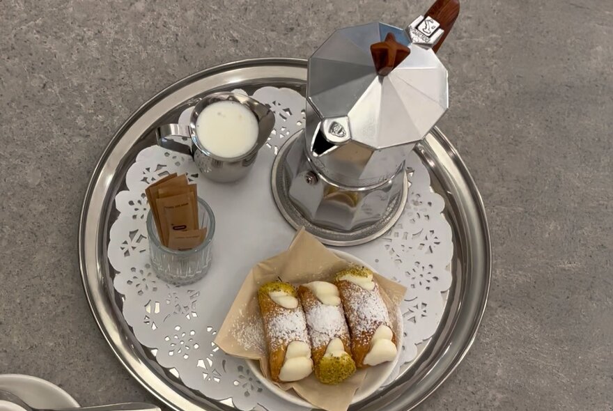 A silver tray with a moka coffee pot, milk and three cannoli.