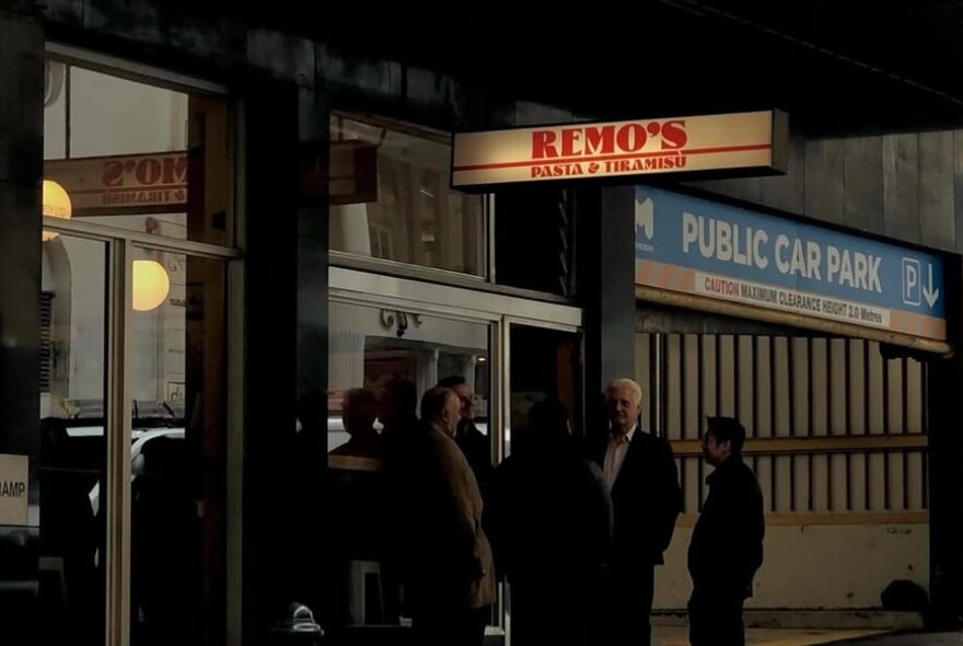The shopfront of Remo's Pasta & Tiramisu restaurant, with a group of older Italian men standing outside.