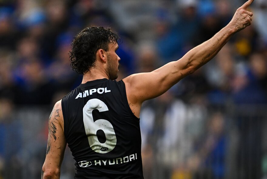 A Carlton AFL football player, seen from behind, with his right arm raised above him.