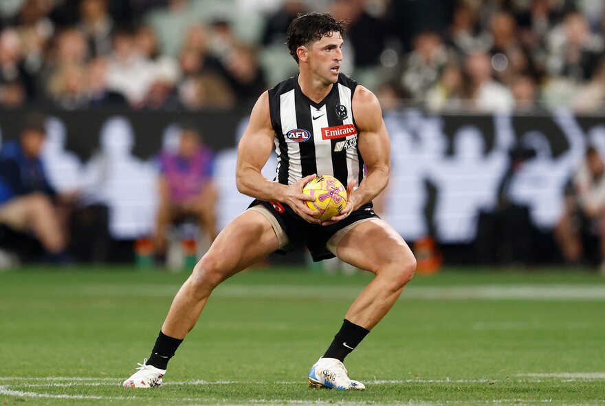 A Collingwood AFL football player on the field with the ball during a match.