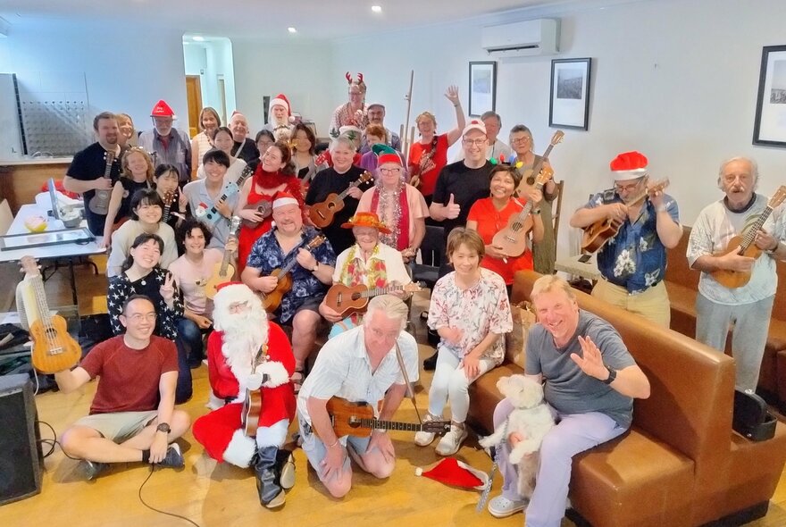 A large group of people all holding ukeleles as they pose for a photo in a white-walled room.