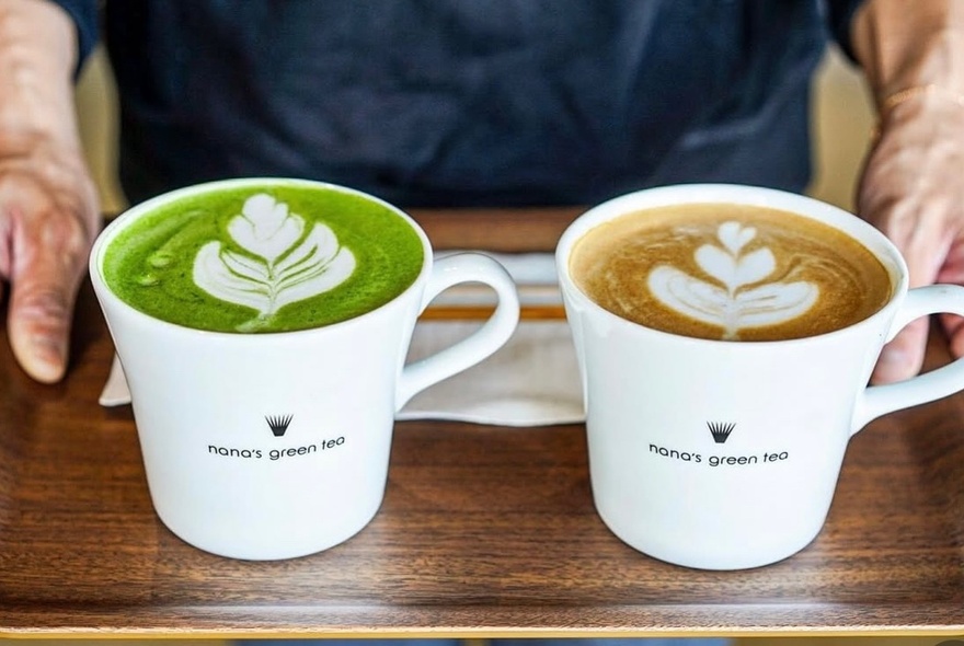 Hands holding a tray with mugs of green tea and coffee.