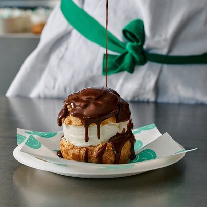 A gelato-filled profiterole with chocolate sauce being drizzled over it.