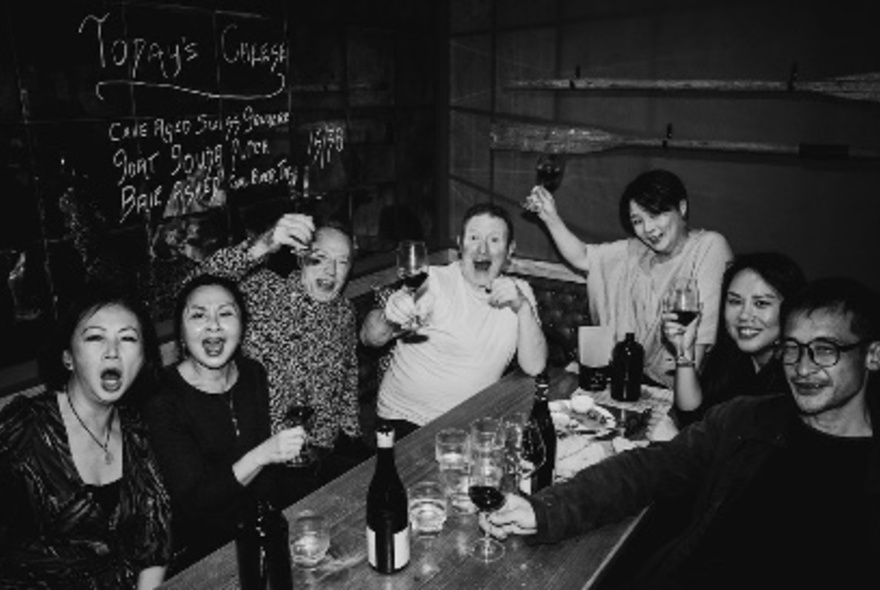 A table of people at a wine bar enjoying themselves, eating and drinking; black and white image.