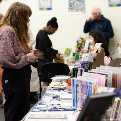 A community book fair event, featuring tables lined with independent publications, with attendees browsing and interacting with stallholders.