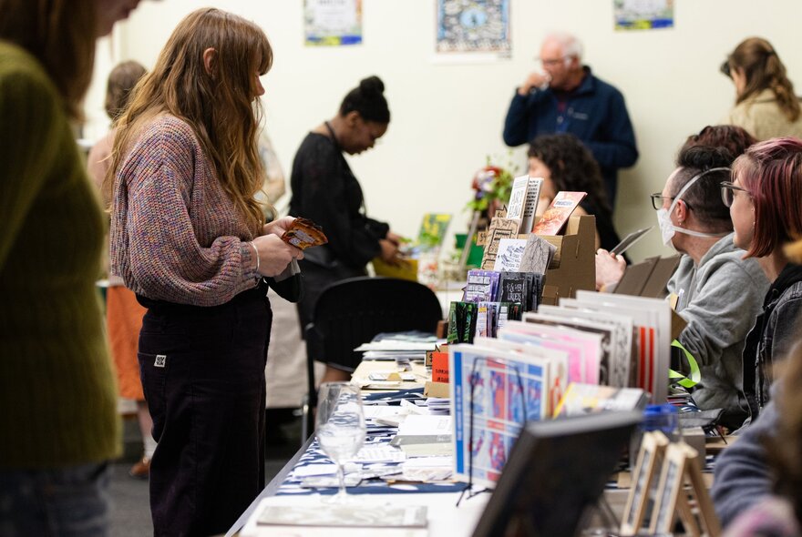 A community book fair event, featuring tables lined with independent publications, with attendees browsing and interacting with stallholders.