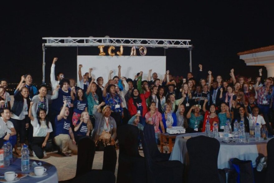 A room of people all facing forward and holding a fist in the air. 