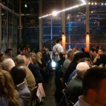 The dining room at Taxi Kitchen filled with people eating and drinking at tables, with large windows looking out onto the night sky.