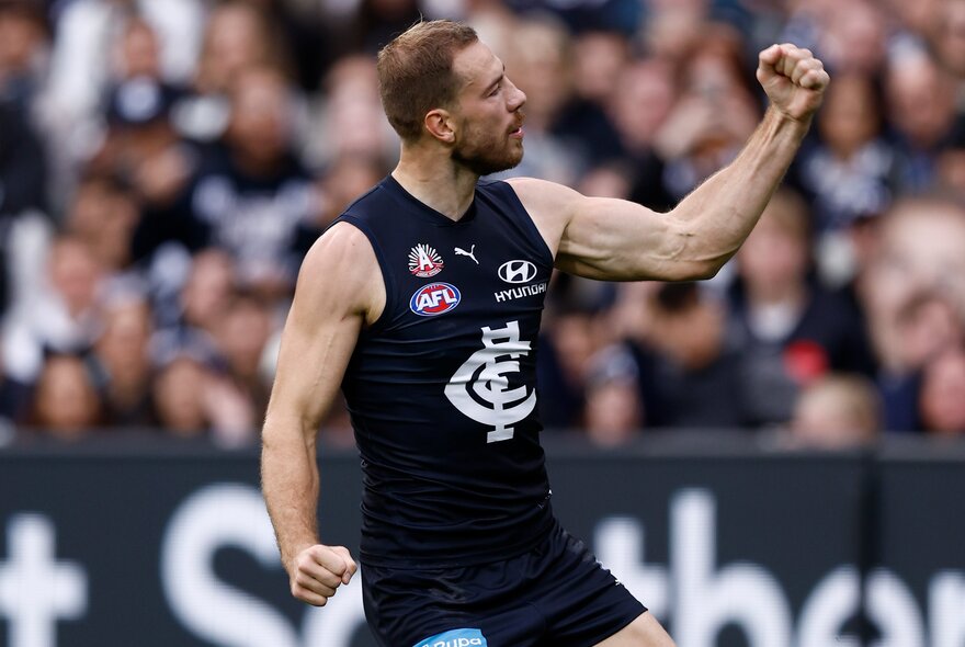 Carlton AFL football player with arms outstretched during a match.