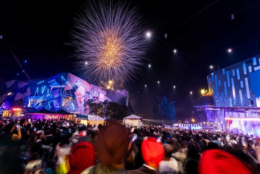 Night view of Fed Square with a crowd of people enjoying a fireworks display over the Fed Square buildings.