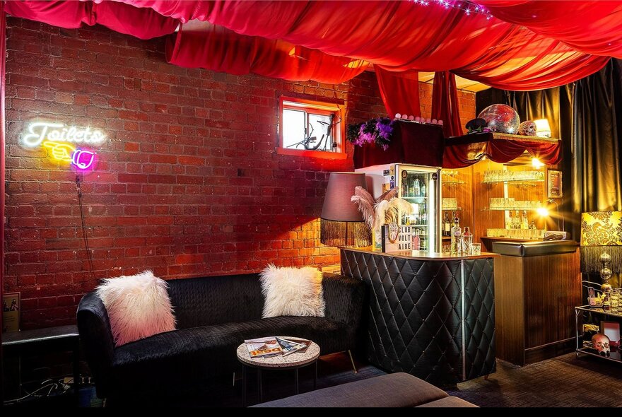 The cosy, intimate bar and lobby area of Club Voltaire with a black couch, soft lighting and billowing red fabric suspended across the ceiling.