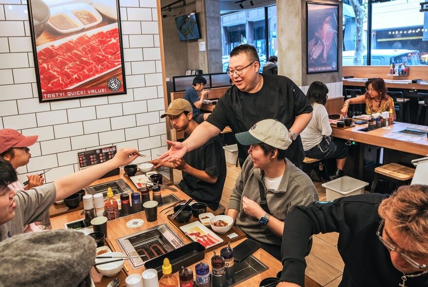 People in a restaurant enjoying Japanese-style barbecue, grilling various meats and vegetables over a tabletop grill.