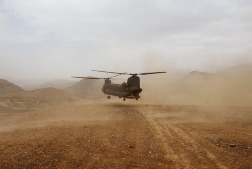 An Australian Army helicopter landing in a dusty and deserted landscape.