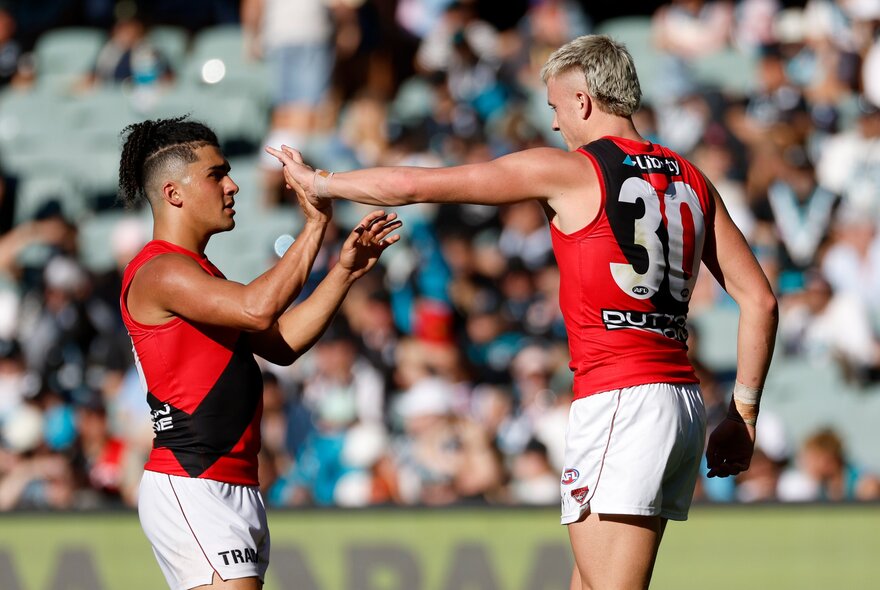 Essendon AFL football players on the field during a match giving each other a high five.