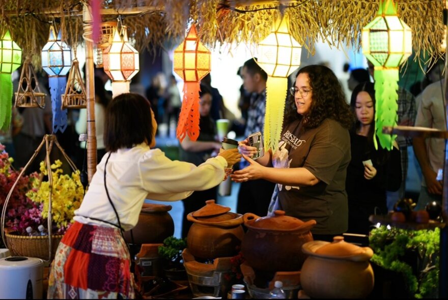 A woman selling produce from earthenware pots at an Asian-style night market.