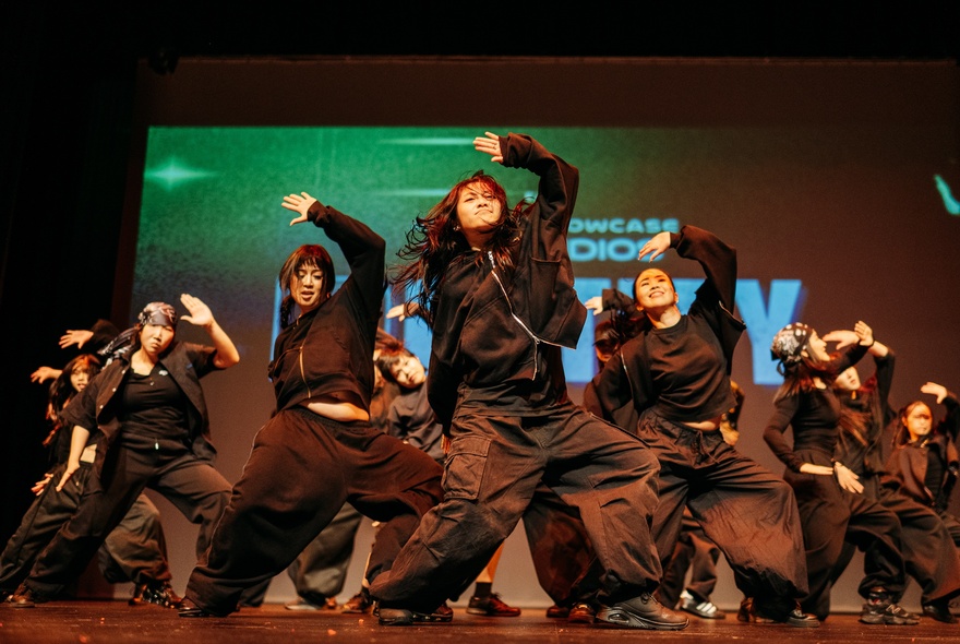 Group of dancers performing on stage wearing black.