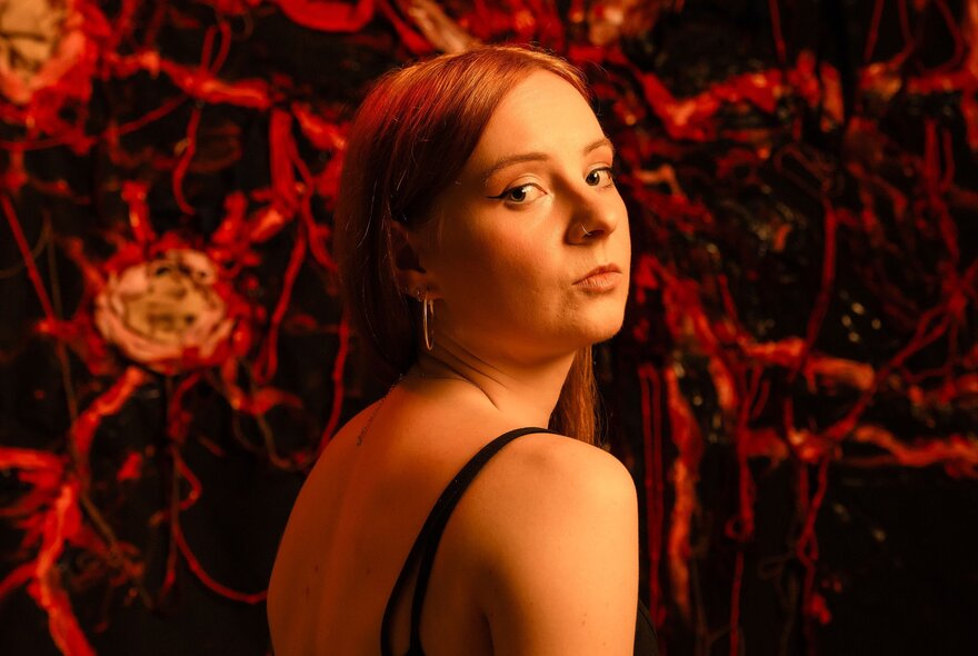 A young woman looking over her shoulder with disdain against a complex dark background of red and black. 