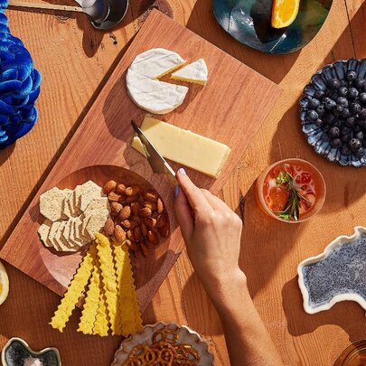 A hand cutting cheese on a large cheeseboard