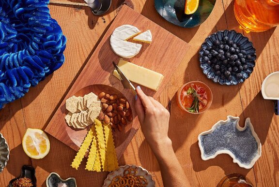 A hand cutting cheese on a large cheeseboard