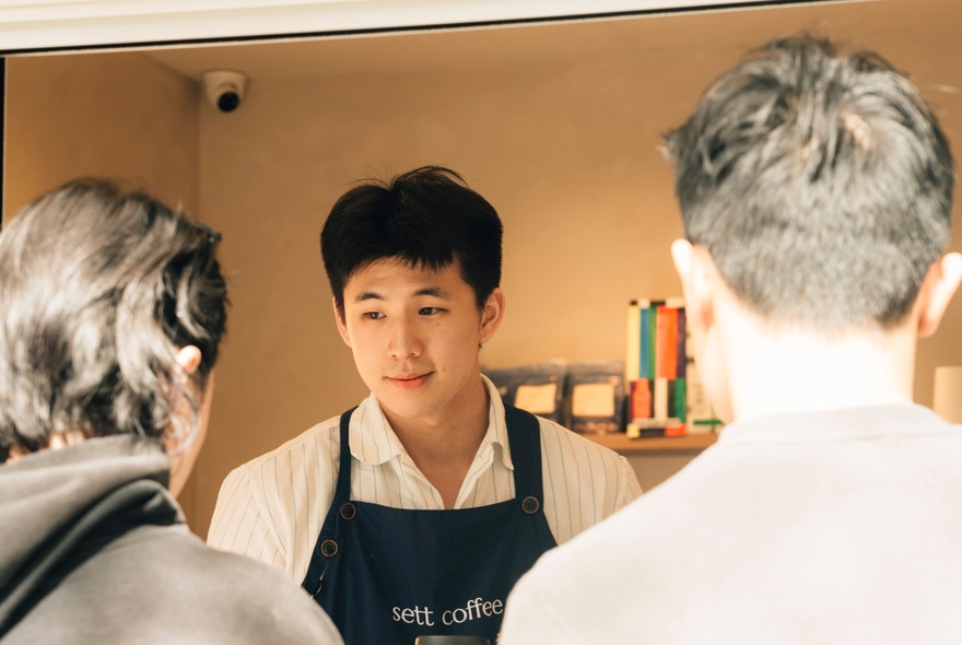 A barista in an apron in front of two customers. 