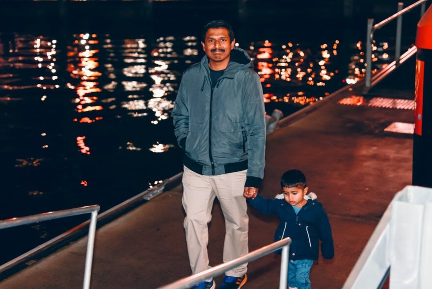 A father and young son walking hand in hand, about to board a boat at a watery berth.