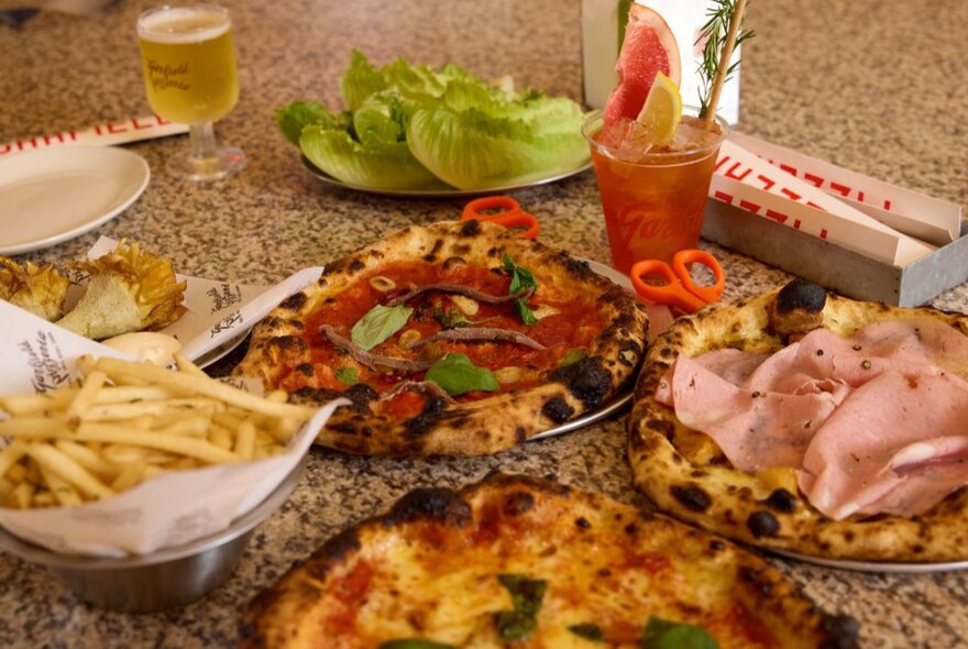 Table of pizzas, chips and drinks.